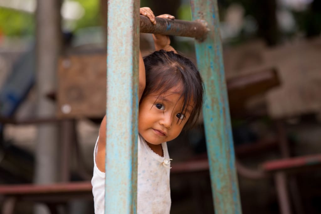 Close-up of a young girl hanging off of a bar looking at the camera.