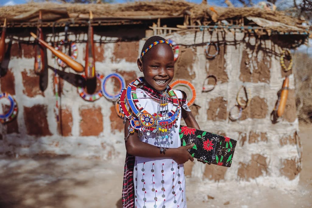 Little girl is standing outside her home and is wearing colorful traditional clothing and jewelry. She is holding a wrapped Christmas gift.