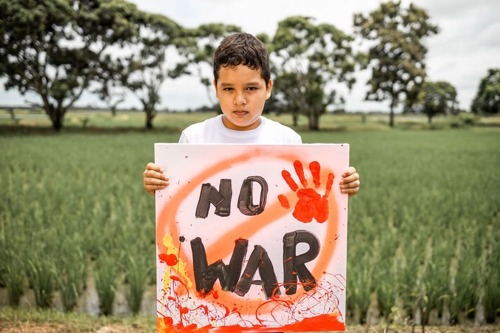 Boy standing with a sign that says: "no war"