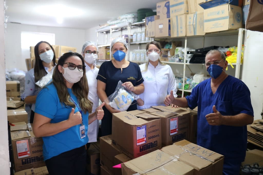 A group, all wearing masks, stand in a storage room amongst boxes of donated supplies.