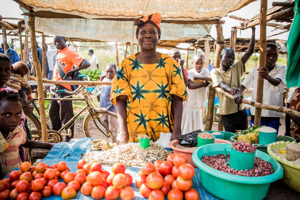 A Ugandan woman stands in front of her stad of vegetable seeds and tomatoes