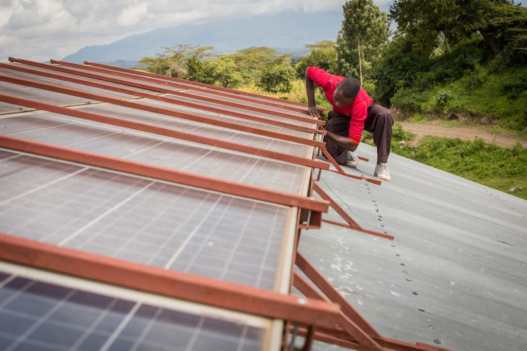 A man in a red shirt works on some solar panels. Solar Panels are one of the gifts in the Gifts of Compassion gift guide.