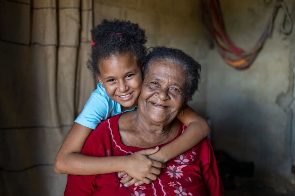 An older woman smiles at the camera while a young girl wraps her arms around her and smiles.