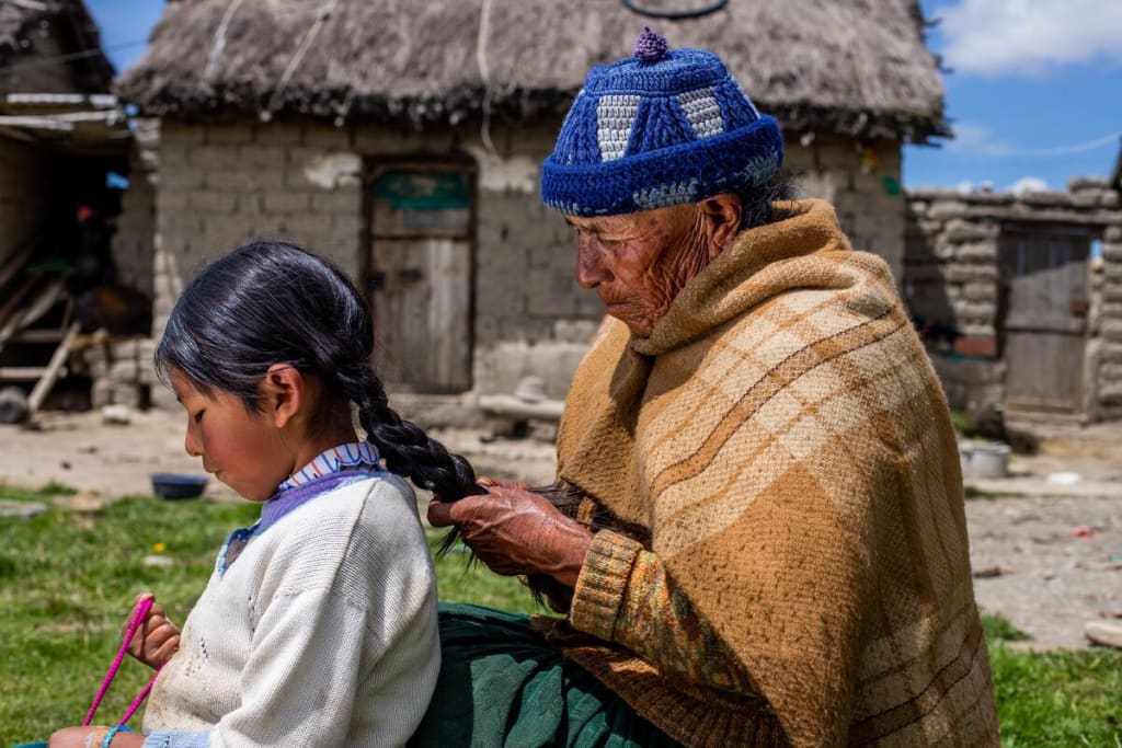 An older woman braids a young girls hair.