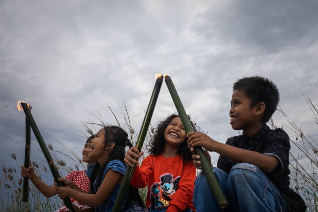 A group of children hold up torches and smile