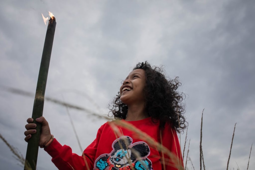 A girl in a red sweater smiles up at a torch she is holding