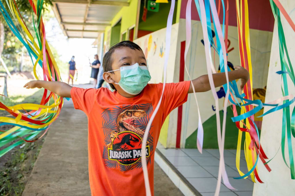 A boy in a orange shirt and a face mask runs through colourful streamers
