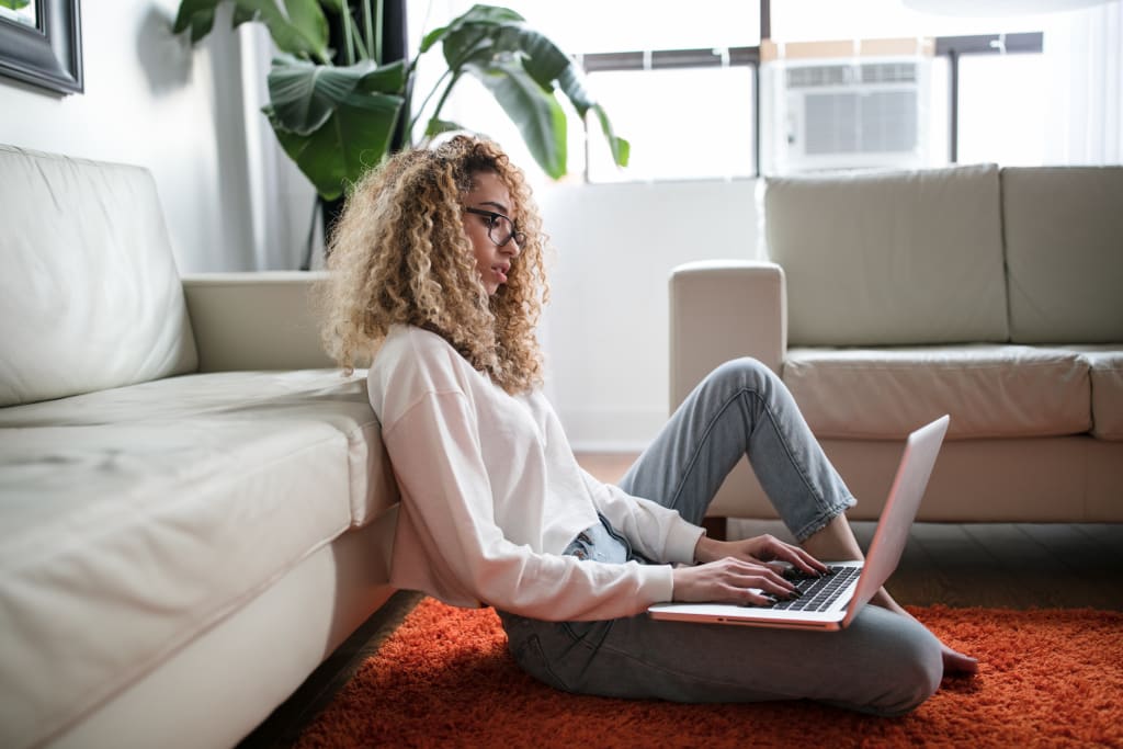 A woman with blonde curly hair sits on the ground with a laptop