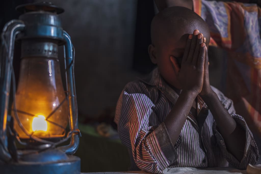 Little boy clasps his hands in prayer by a lamp