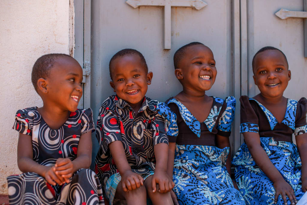 Four little African children sit outside a church door dressed in colorful clothing