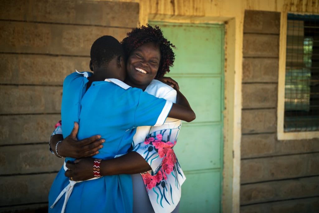 A middle-aged Kenyan woman hugging a teenage school girl in her blue uniform