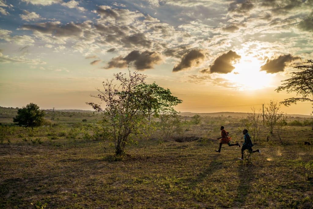 A landscape of a sunset with two children running on the horizon