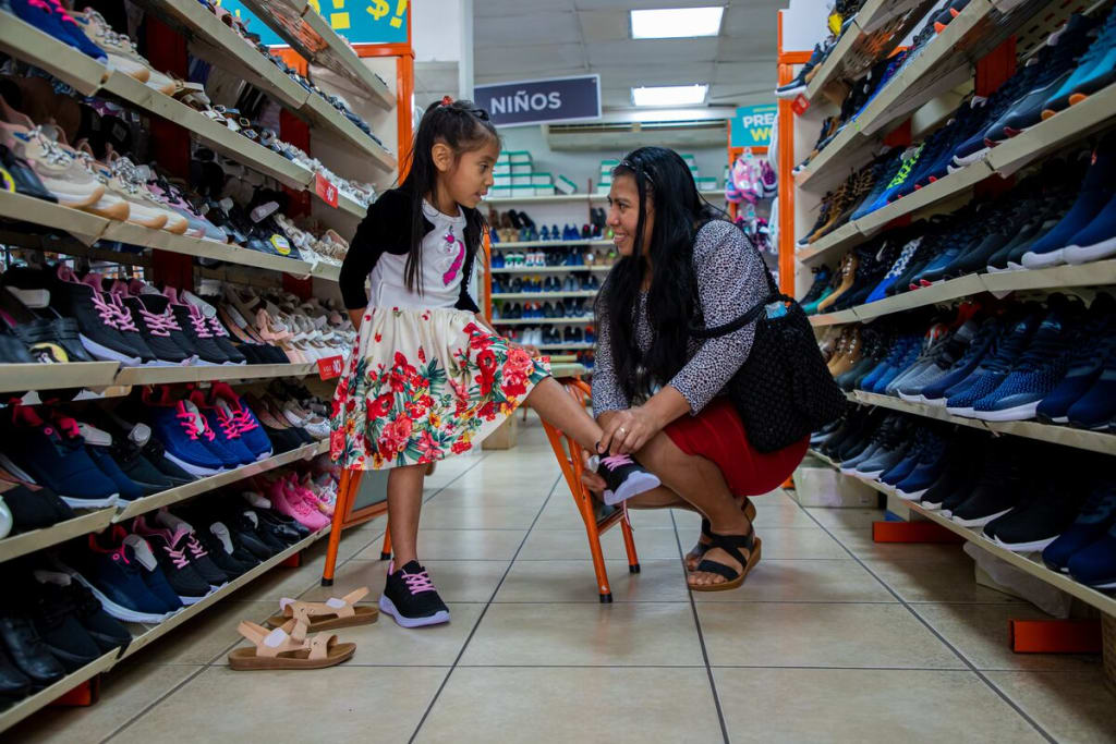 A girl in a colourful dress tries on shoes with her mother who is helping