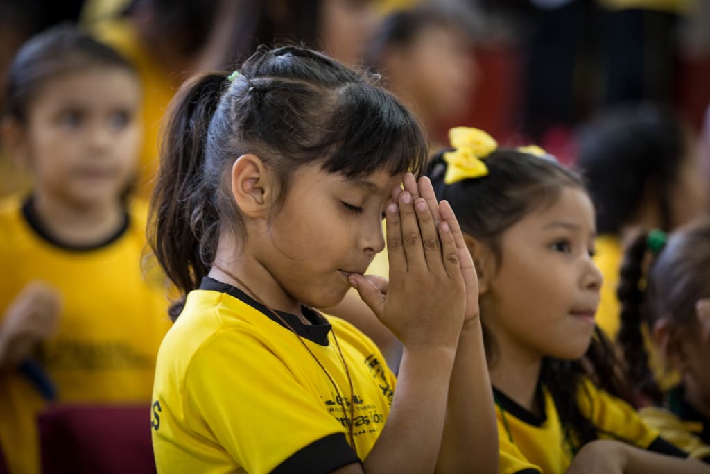 A little girl wearing a yellow t-shirt clasps hands together and closes eyes during prayer
