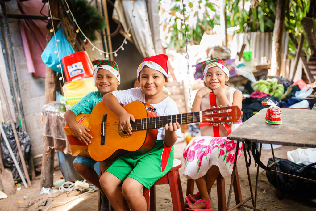 Three children wearing Christmas costumes playing instruments and smiling