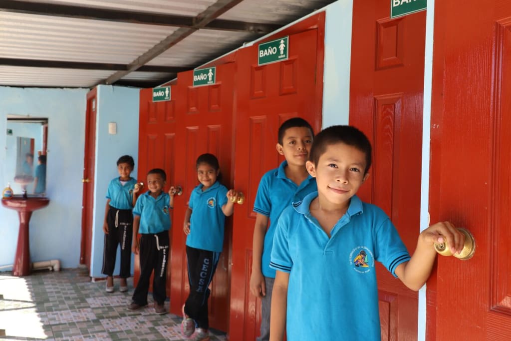 A row of boys in blue shirts stand in front of red doors