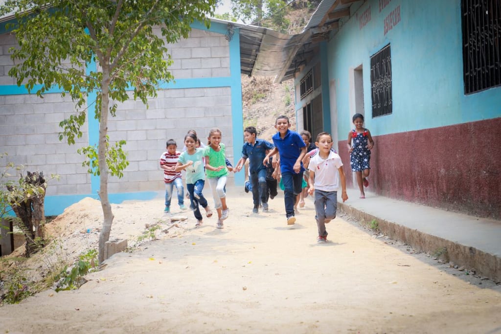 A group of children run towards the camera beside a washroom block