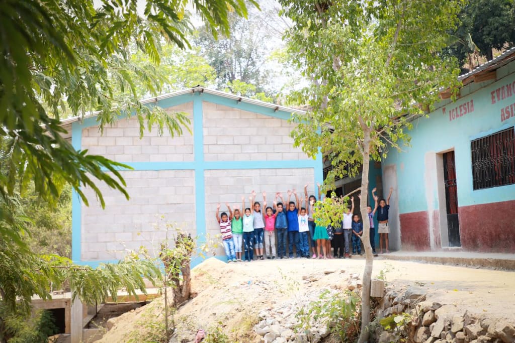 A group of children stand with their hands raised outside of a washroom block