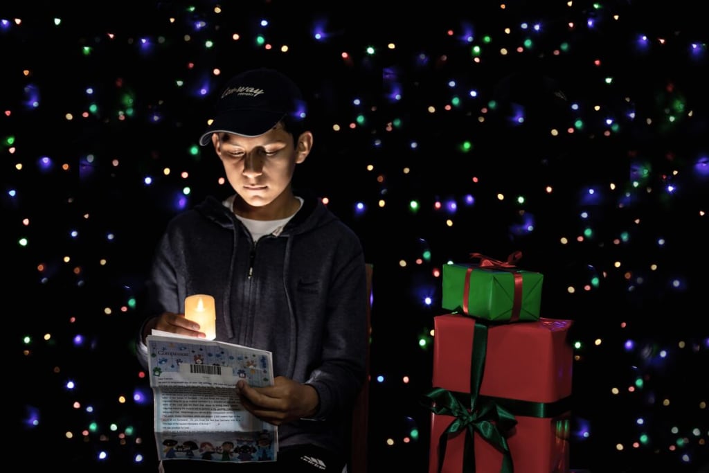A boy in black wearing a baseball cap reads a letter with a candle