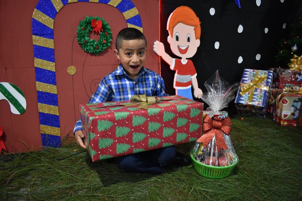 A boy in a blue plaid shirt holds a red present and looks surprised