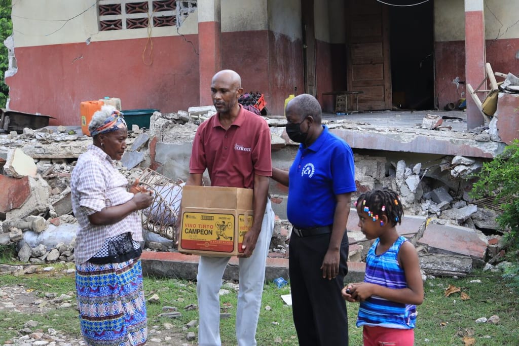 A man in a red shirt carries a box of food to a small group of people