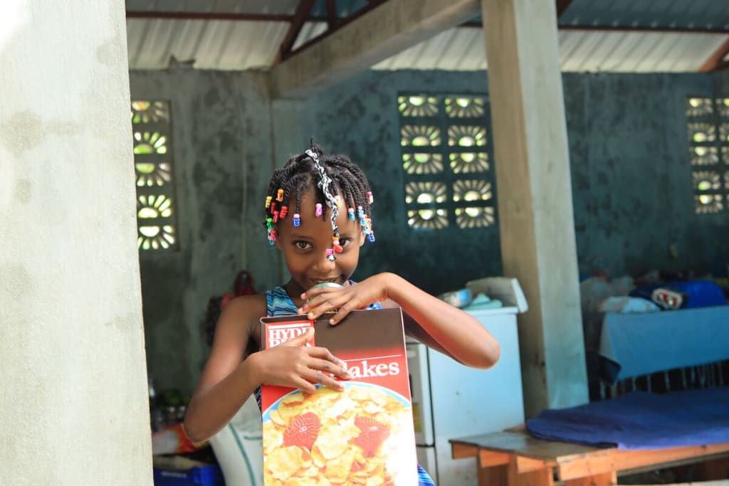A girl smiles at the camera while holding a box of cereal