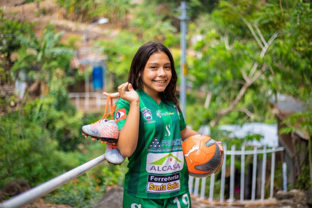 A young girl smiling while holding her soccer equipment.