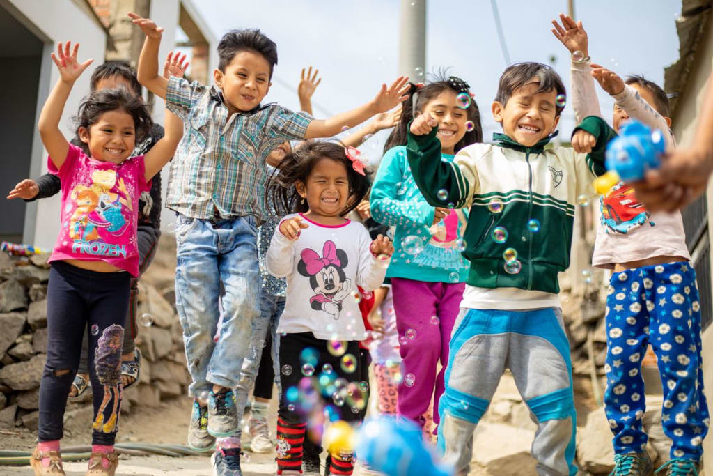 A large group of children playing with bubbles outside the project. They are happy and smiling, and jumping with their arms up.