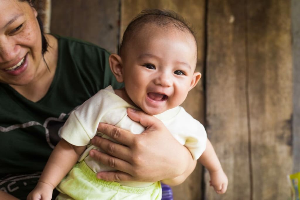 A baby is smiling at the camera in front of a wooden wall.