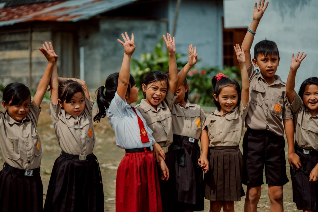 A group of Indonesian children in uniforms raising their hands