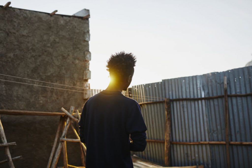 Young man walks passed a brick wall with the sun peaking through.