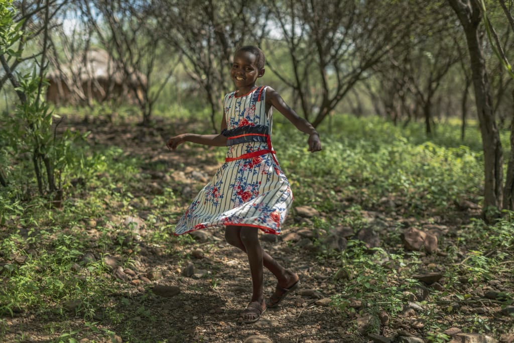 little Kenyan girl twirls around in her dress while surrounded by trees and greenery