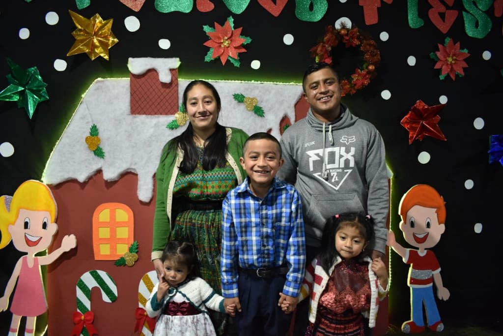 A family of five stands in front of a Christmas display and smiles at the camera