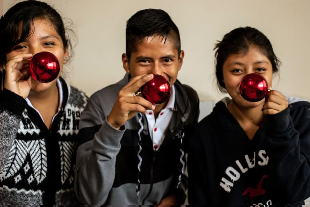 Three teens hold red Christmas ornaments up to their noses and smile.
