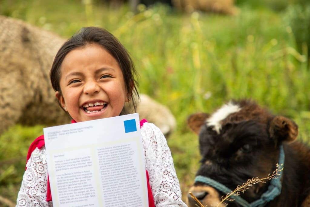 Little girl holds her letter up to the camera, and a cow is in the corner.