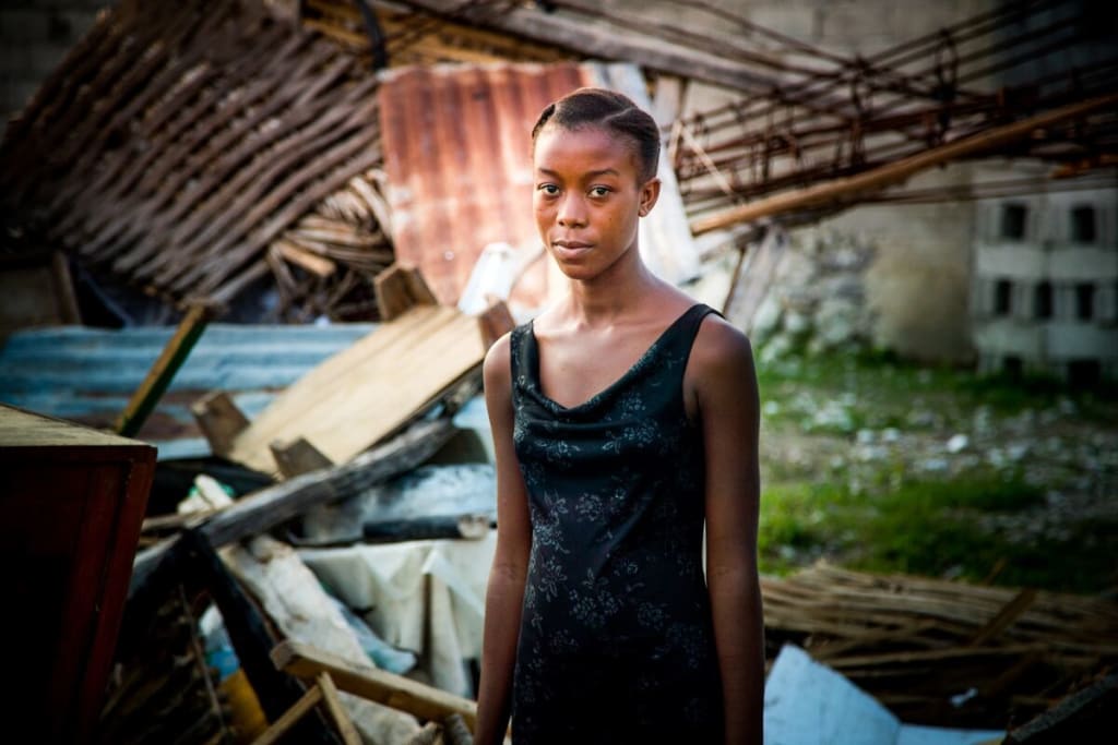 A teenage girl stands in front of a destroyed home