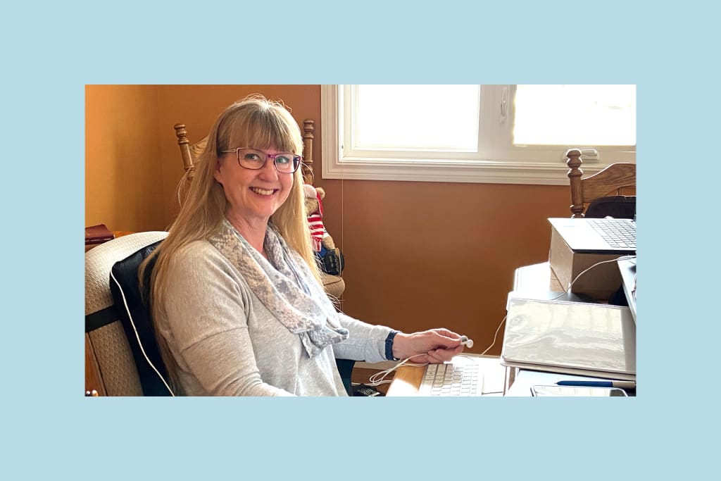 Lynda is wearing glasses and a grey sweater, sitting at her desk in her home office.