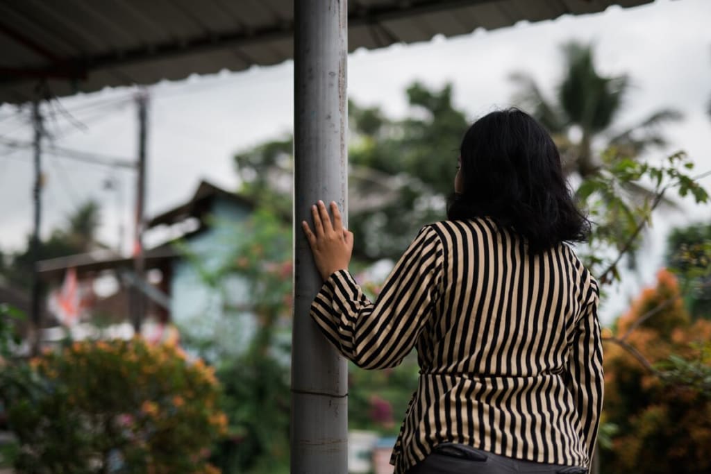 Girl in a stripped shirt walks through the street, her hand on a pole.