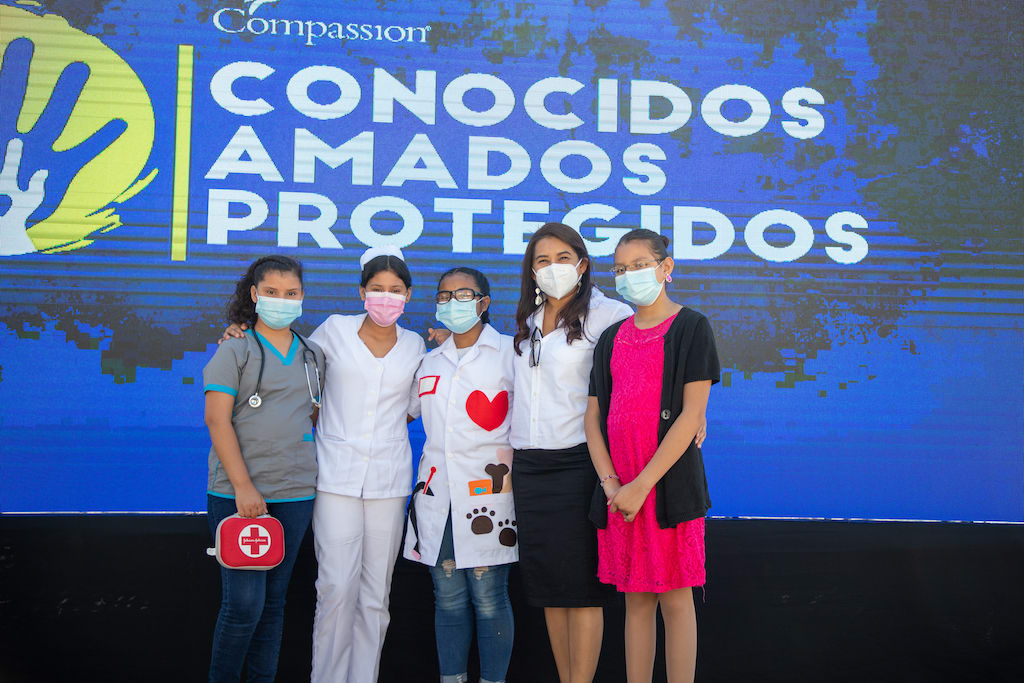 Brenda Rivas, Compassion El Salvador's National Director, with children from ES0793 during a child protection ceremony done to commemorate the children’s rights anniversary. Some children wore traditional dresses and others dressed as professionals according to what they want to be in the future. All of them are wearing face masks.