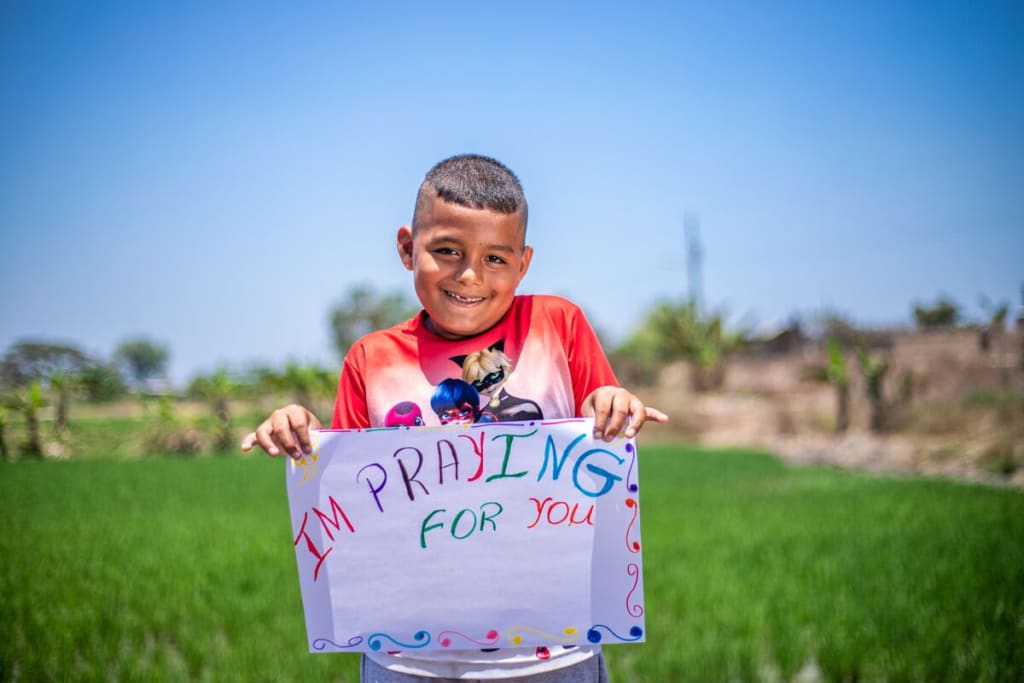Little boy holds a sign that says, "I'm praying for you."