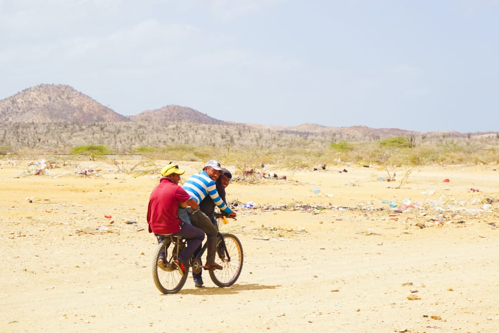 Three men ride on one bike through the desert