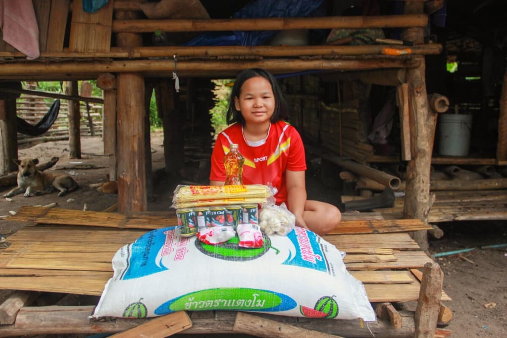 Young girl in red shirt smiles with a big bag of rice and some other food in front of her.