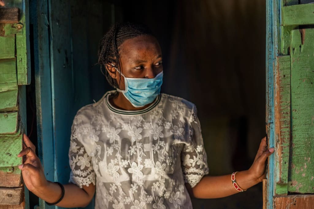 Girl wearing a white shirt and wearing a blue masks walks out of a green door,