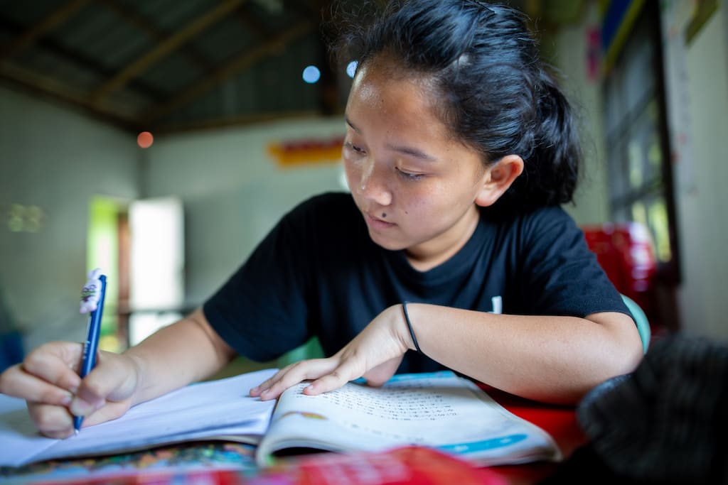A girl sits at a desk writing in a notebook.