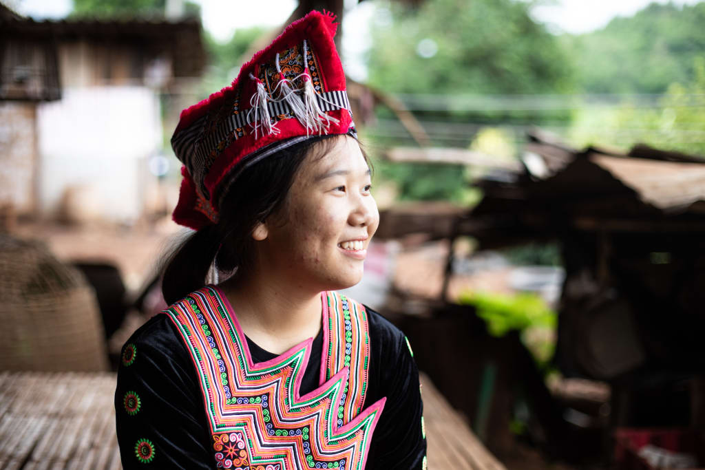 Girl wearing a traditional hat smiles looking off into the distance.