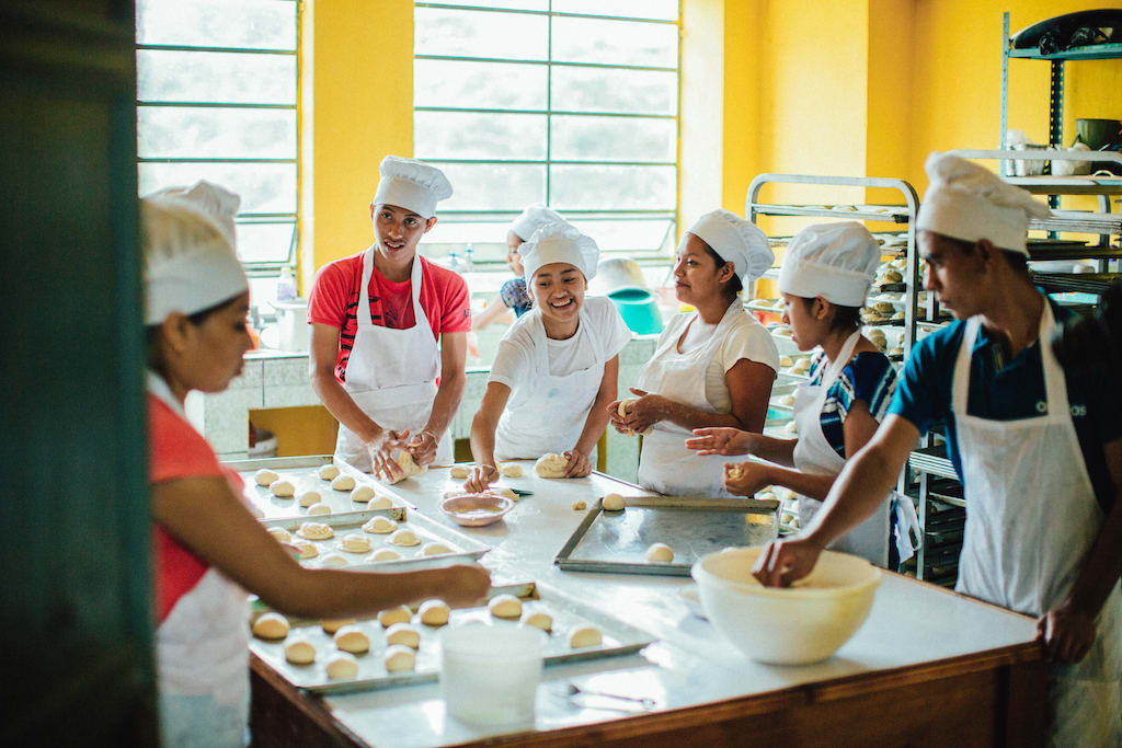 A group of students stand around a kitchen island, placing balls of dough on pans.