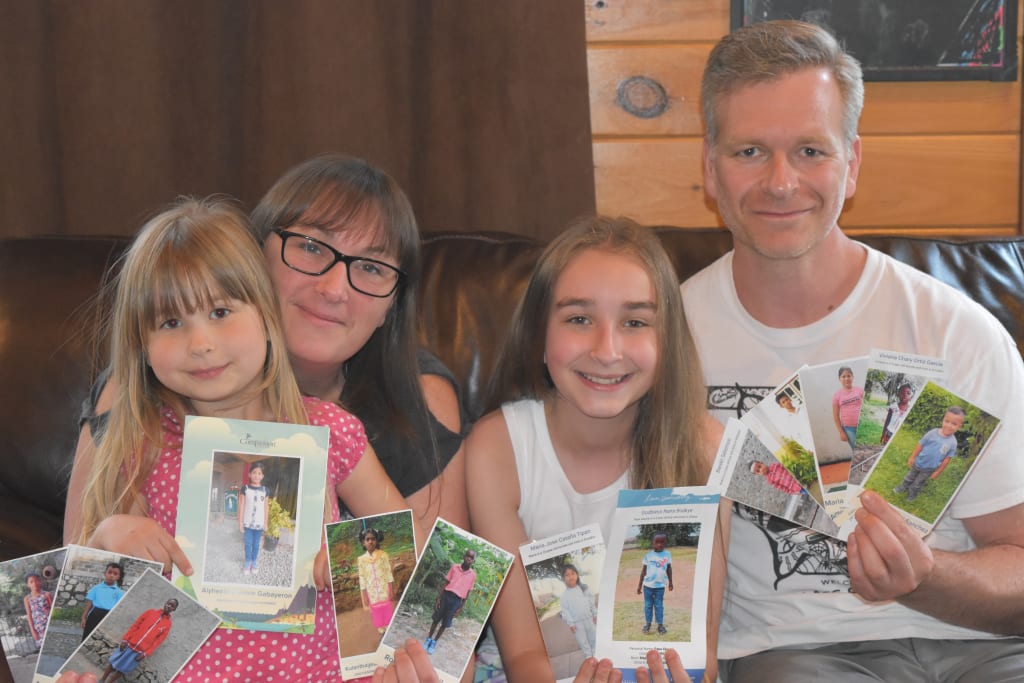 Josh, his wife and his two daughters hold up pictures of their sponsored childen