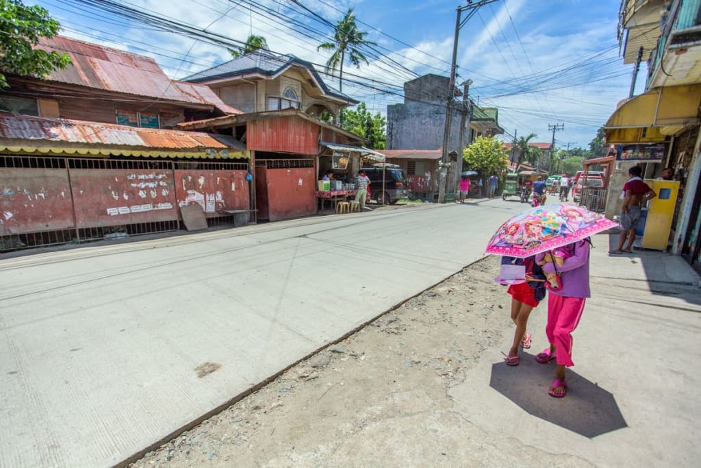 Two girls walk down the street with a pink umbrella covering their faces.