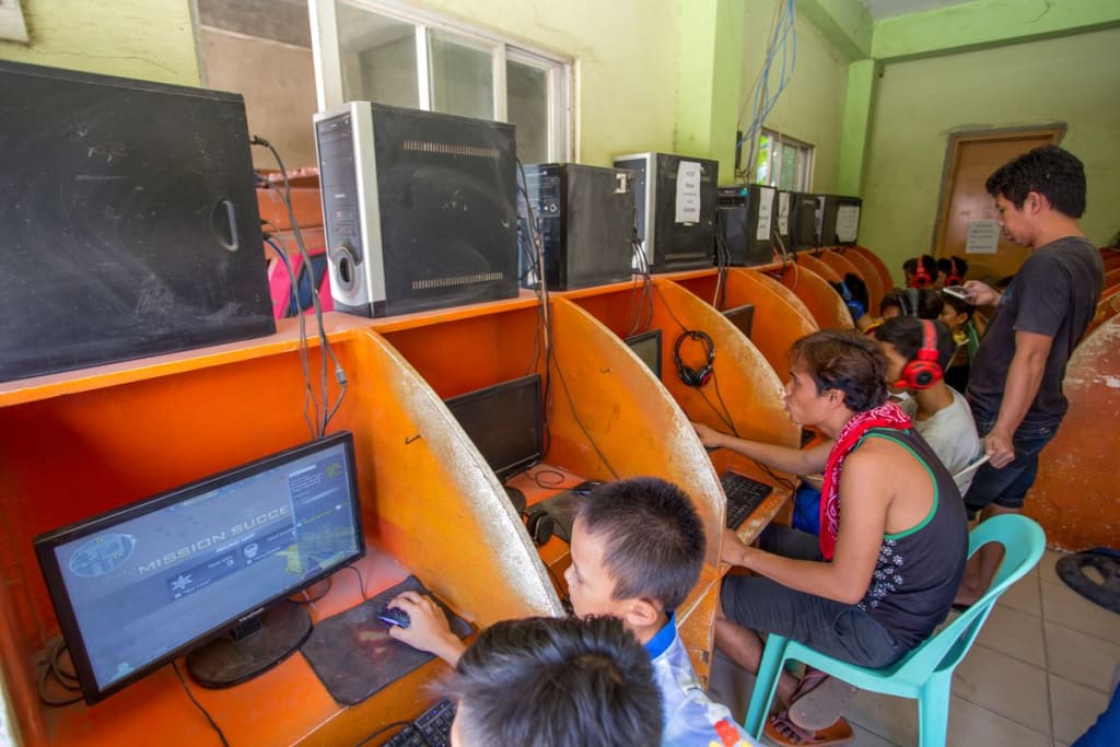 Children and young adults are pictured in orange cubicles in an internet cafe.