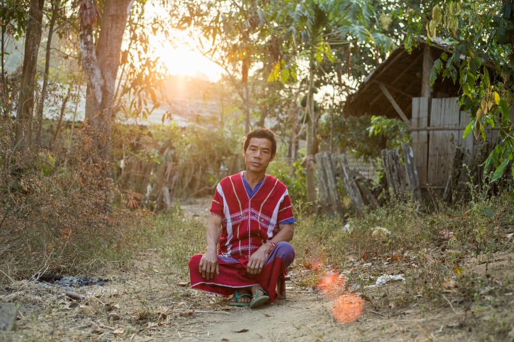 Moue-ae, Thidarat’s father sits cross legged, outside his home, with a serious look on his face.